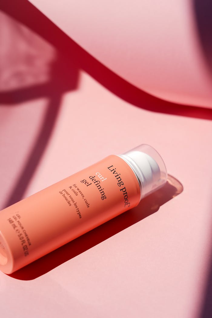 A bottle of Living Proof curl defining hair gel on a pink background with shadow play.